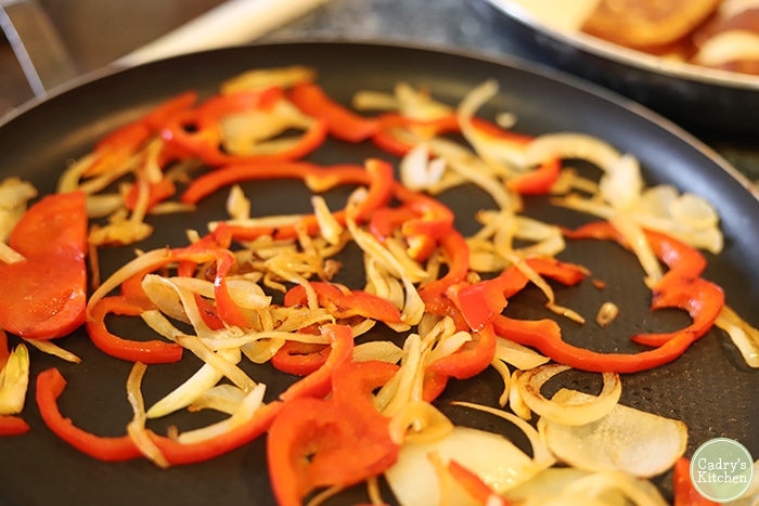 Onions and peppers being sauteed in skillet.