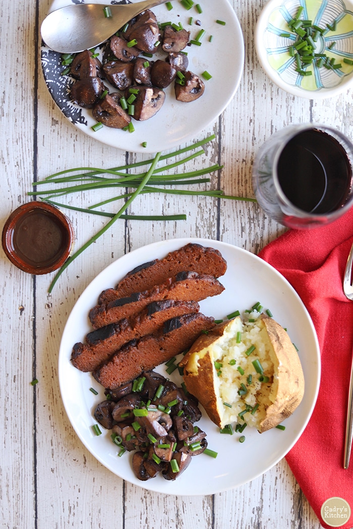 Overhead slices of seitan ribeye steak, baked potato, and red wine mushrooms.