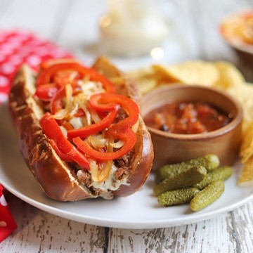 Vegan cheesesteak sandwich on plate with salsa and chips.