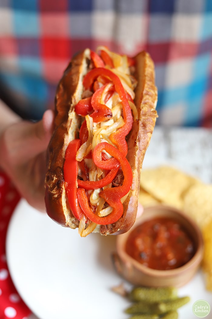 Vegan Philly cheesesteak sandwich in hand, being held over chips & salsa.