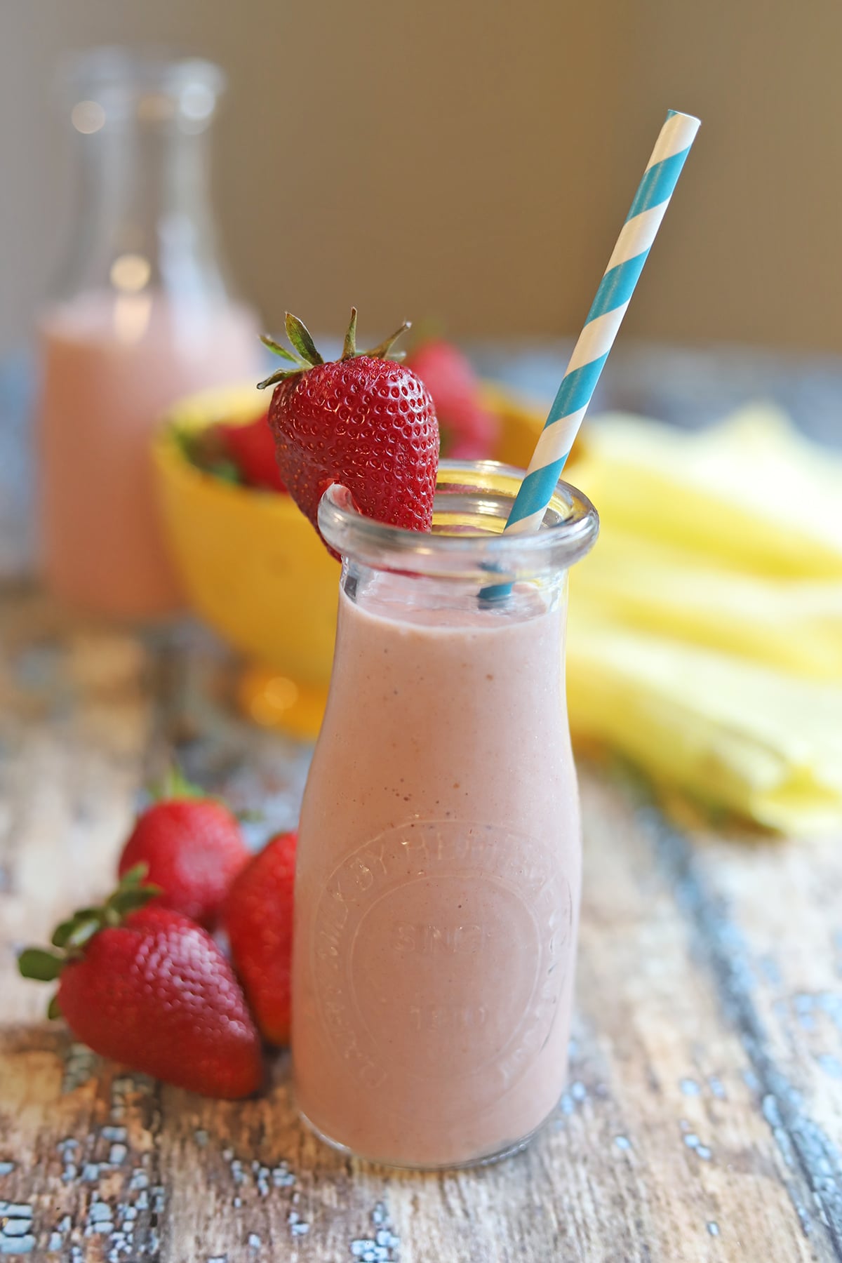 Strawberry milk in tall bottle with straw & strawberries.