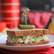 Text overlay: Vegan egg salad. Sandwich on plate skewered by a cornichon.