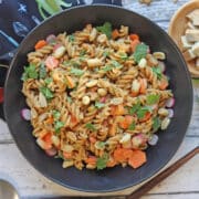 Cold peanut noodles with carrots and cilantro, dressed in peanut sauce, in black bowl.