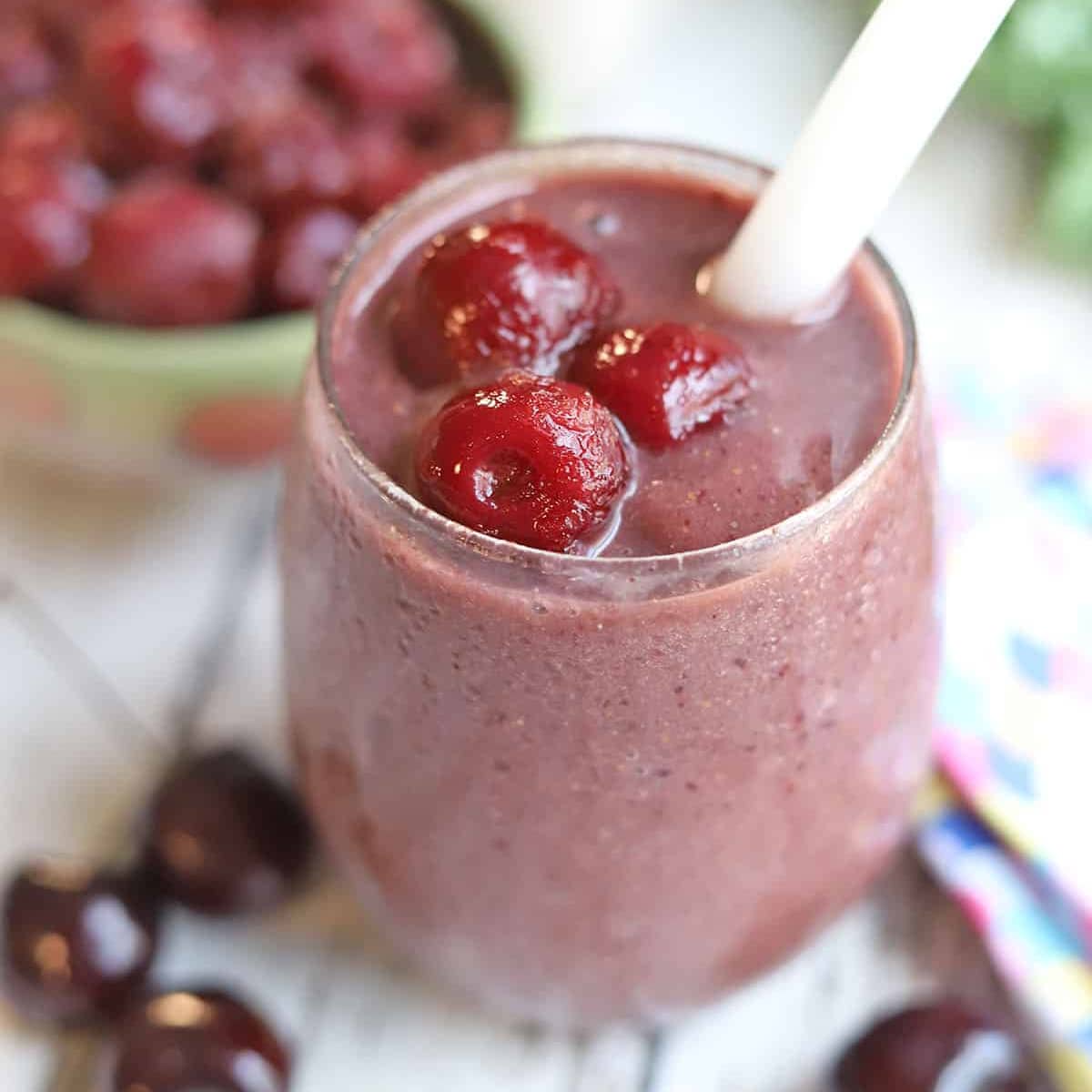 Cherry smoothie garnished with frozen cherries in glass with white straw.