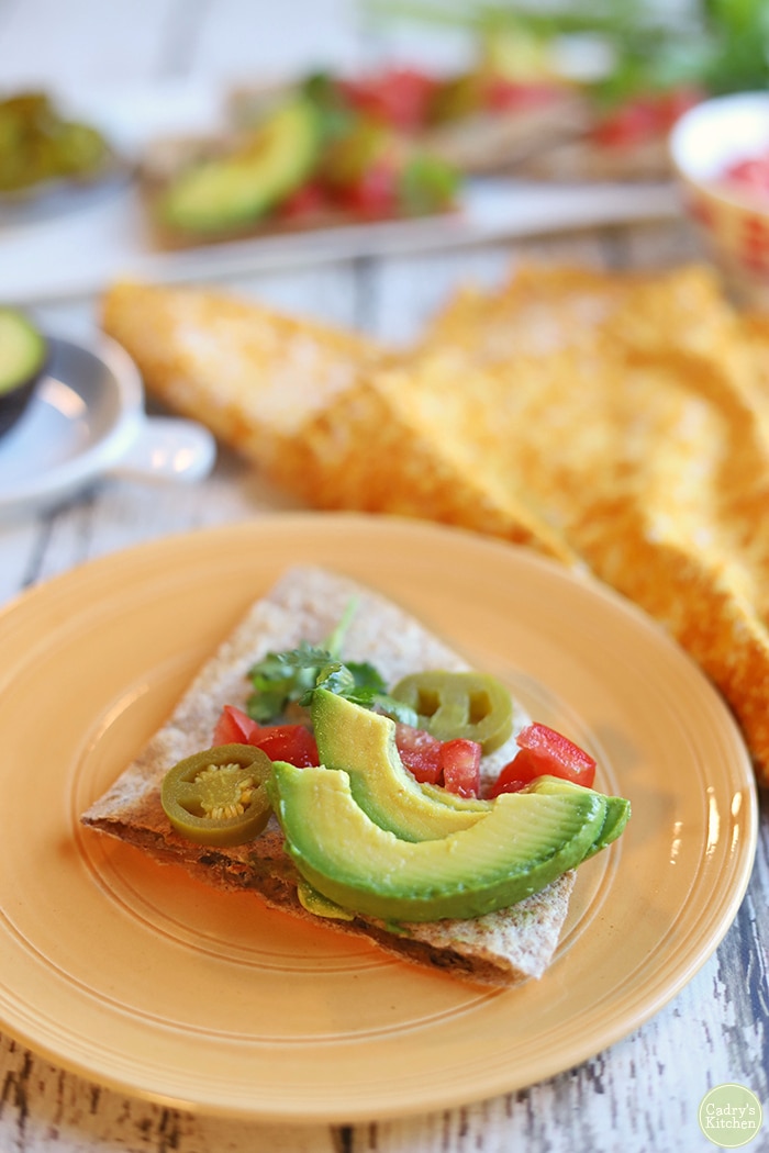 Refried bean quesadilla wedge with avocado, tomatoes, and jalapeno pepper slices.