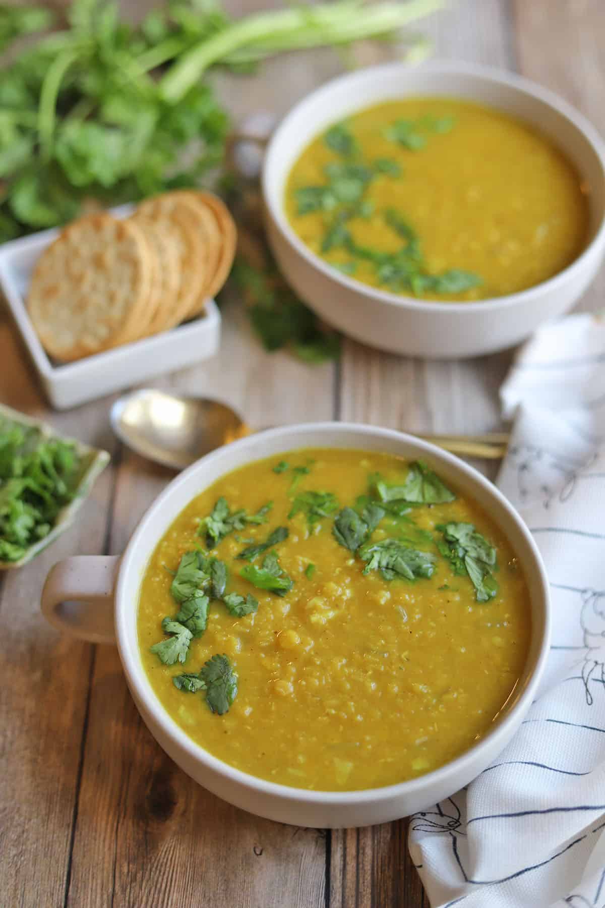 Bowls of curry red lentil soup by cilantro and crackers.