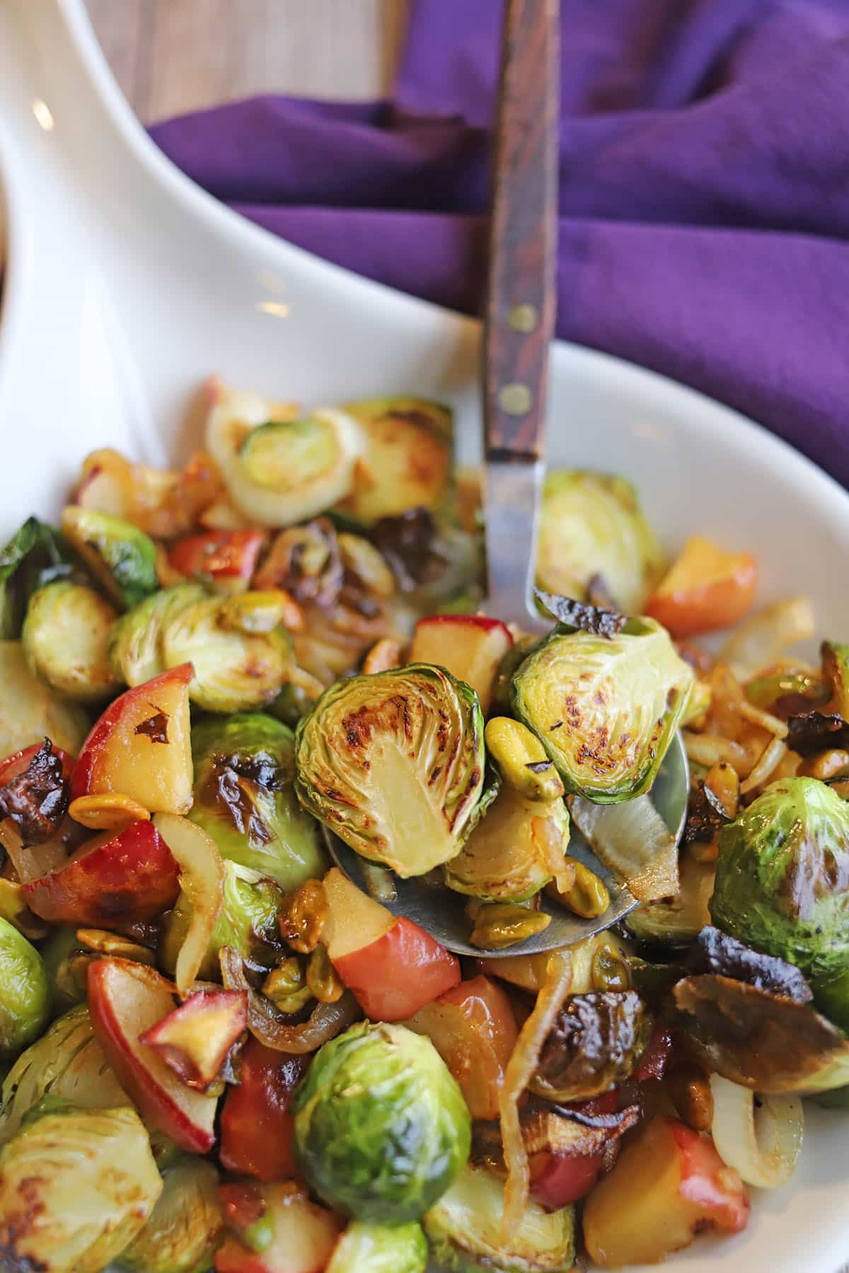 Close-up roasted Brussels sprouts in spoon with caramelized onions & apples.
