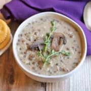 Creamy vegan mushroom soup with lentils in bowl garnisihed with fresh thyme and mushrooms.