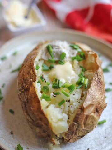 A baked potato topped with chives and non-dairy butter on plate.