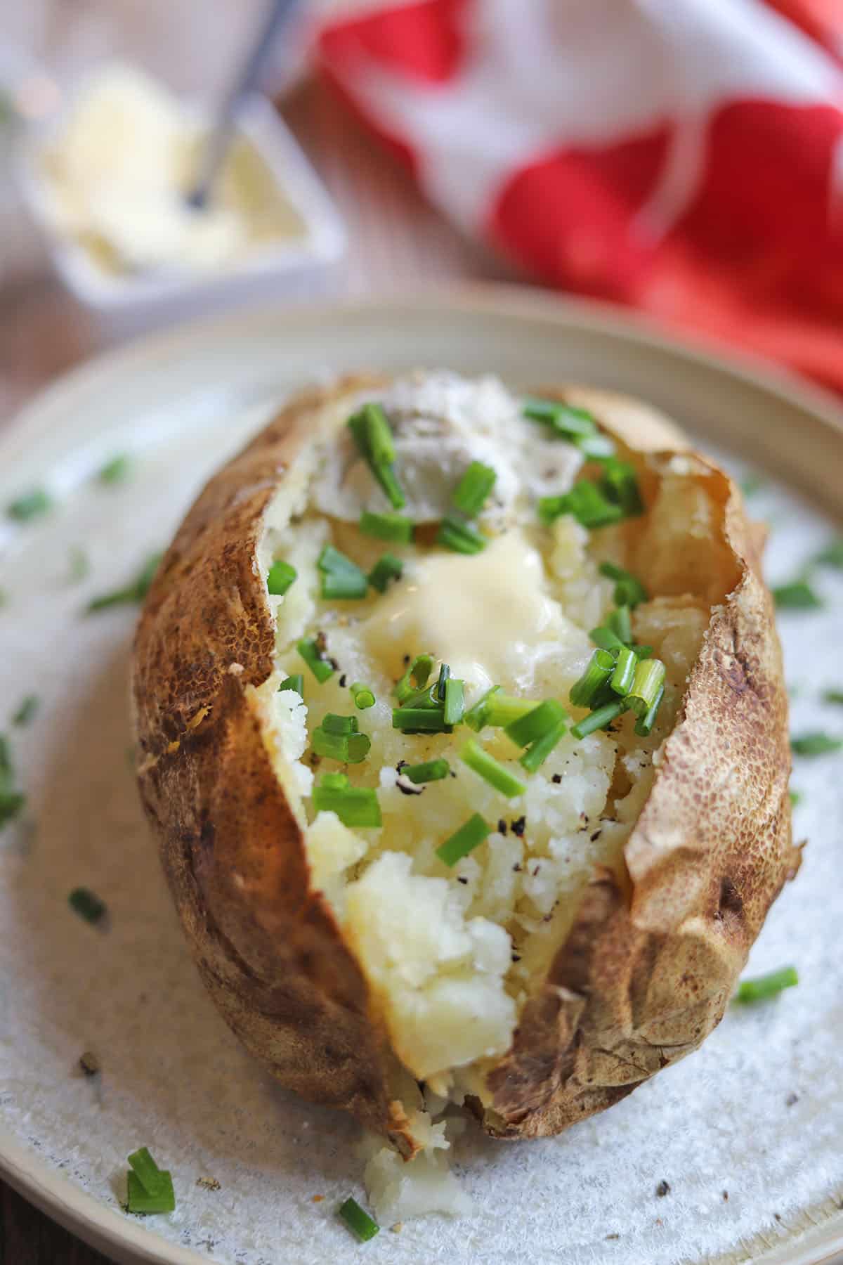A baked potato topped with chives and non-dairy butter on plate.