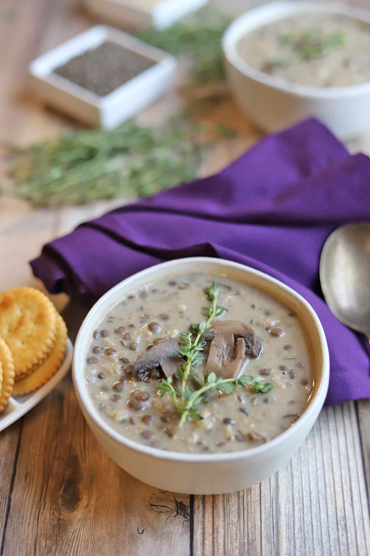 Creamy mushroom lentil soup in bowl by purple napkin and fresh thyme.