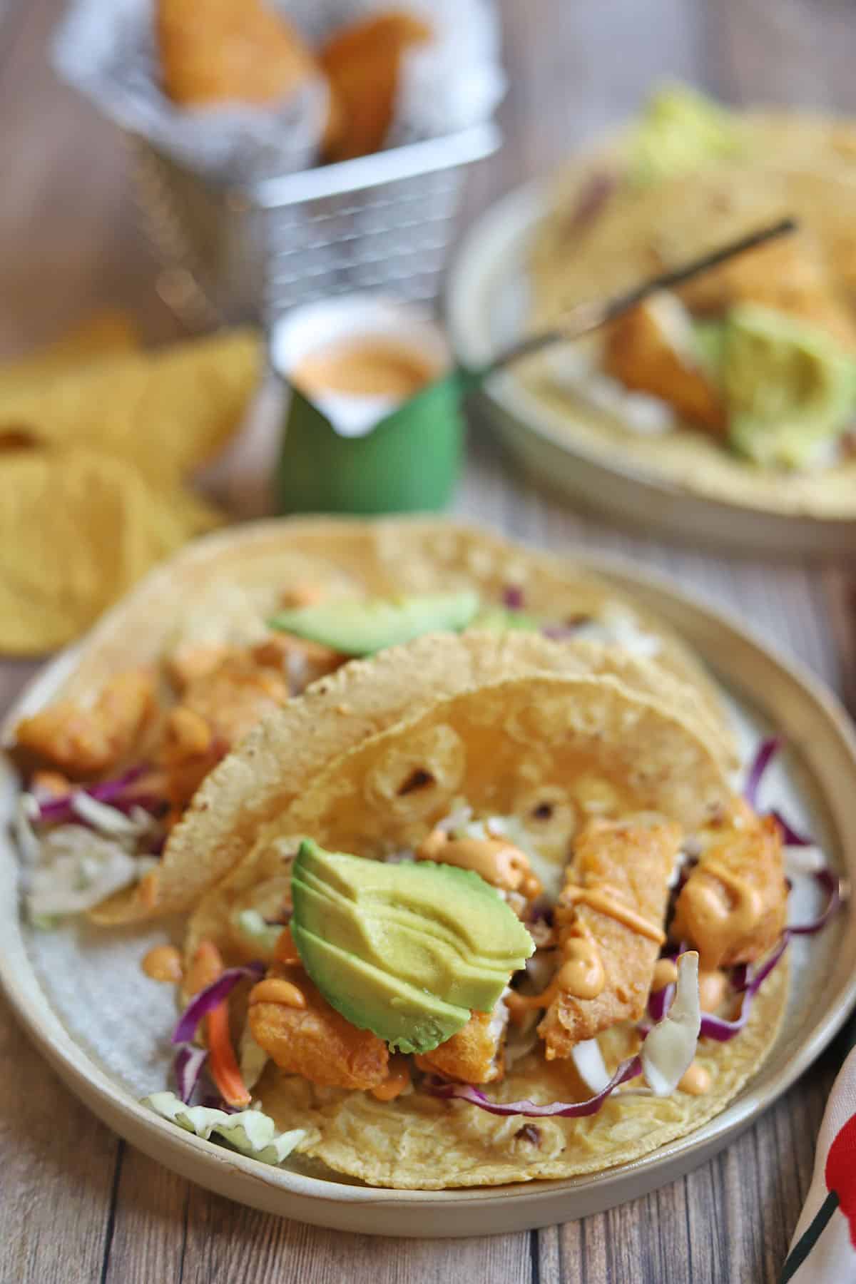 Vegan fish tacos on plates by chipotle crema.