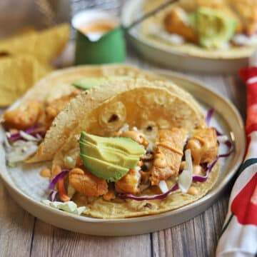 Vegan fish tacos on plates by chipotle crema.
