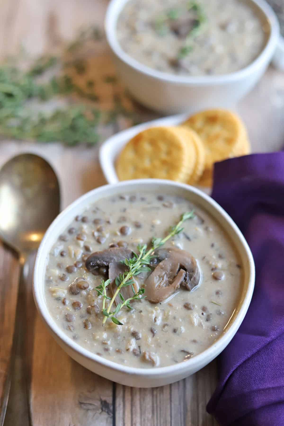 Creamy mushroom lentil soup in bowl by crackers and spoon.