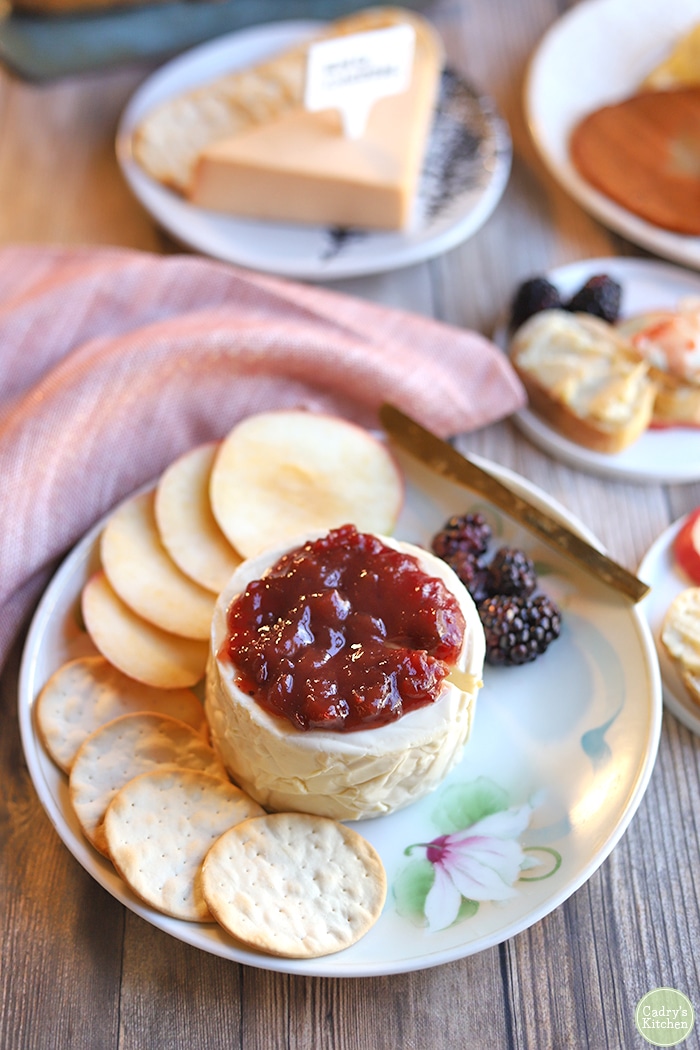 Vegan brie with orange cranberry sauce, apple slices, and crackers on plate.