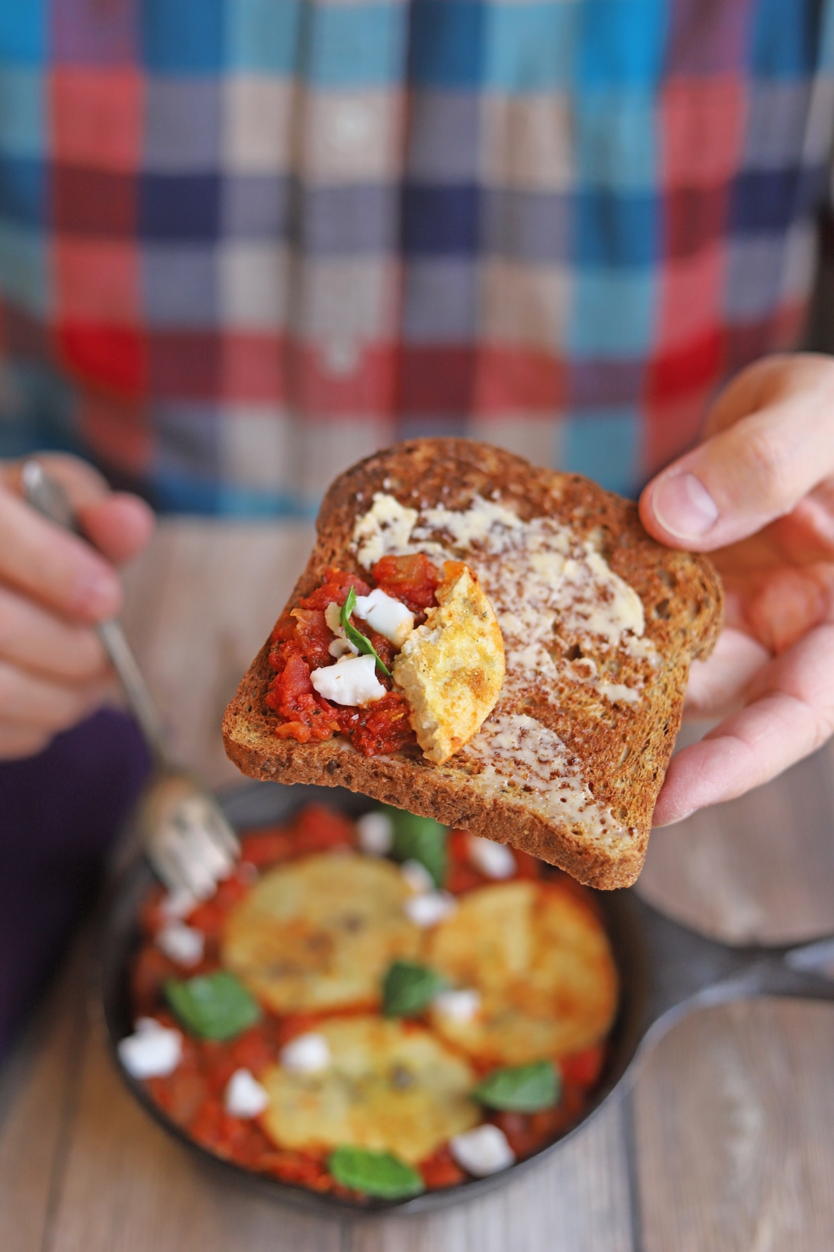 Hand holding buttered toast with eggy tofu and shakshuka.