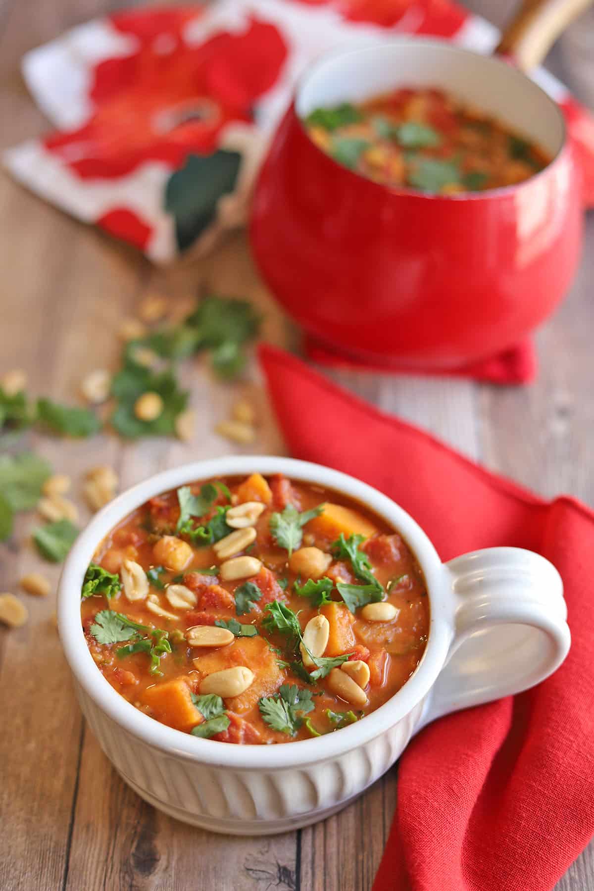 Sweet potato peanut stew in white bowl by red napkin and pot.