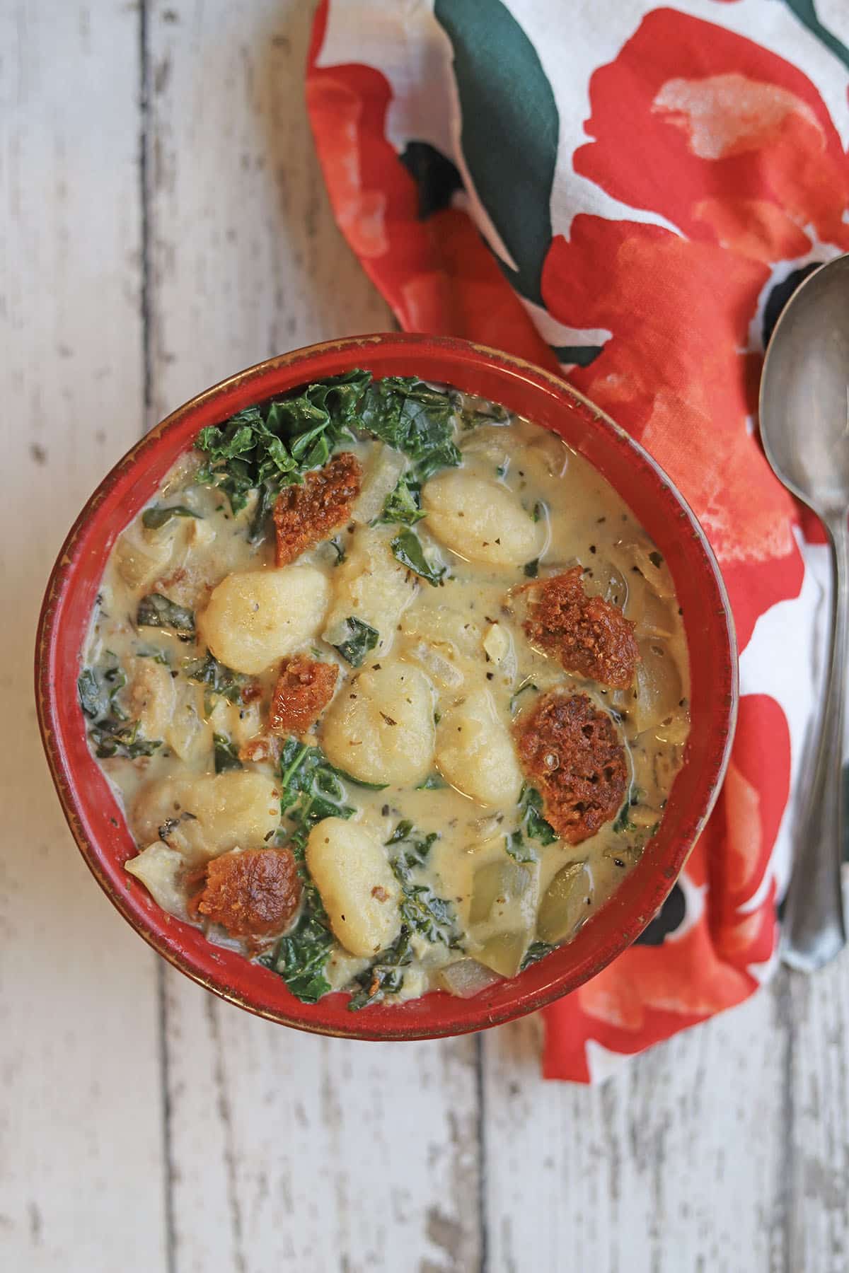 Bowl of vegan soup with gnocchi, sausage and kale by floral napkin.