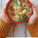 Text overlay: Vegan gnocchi soup with sausage and kale. Hands holding bowl of soup.