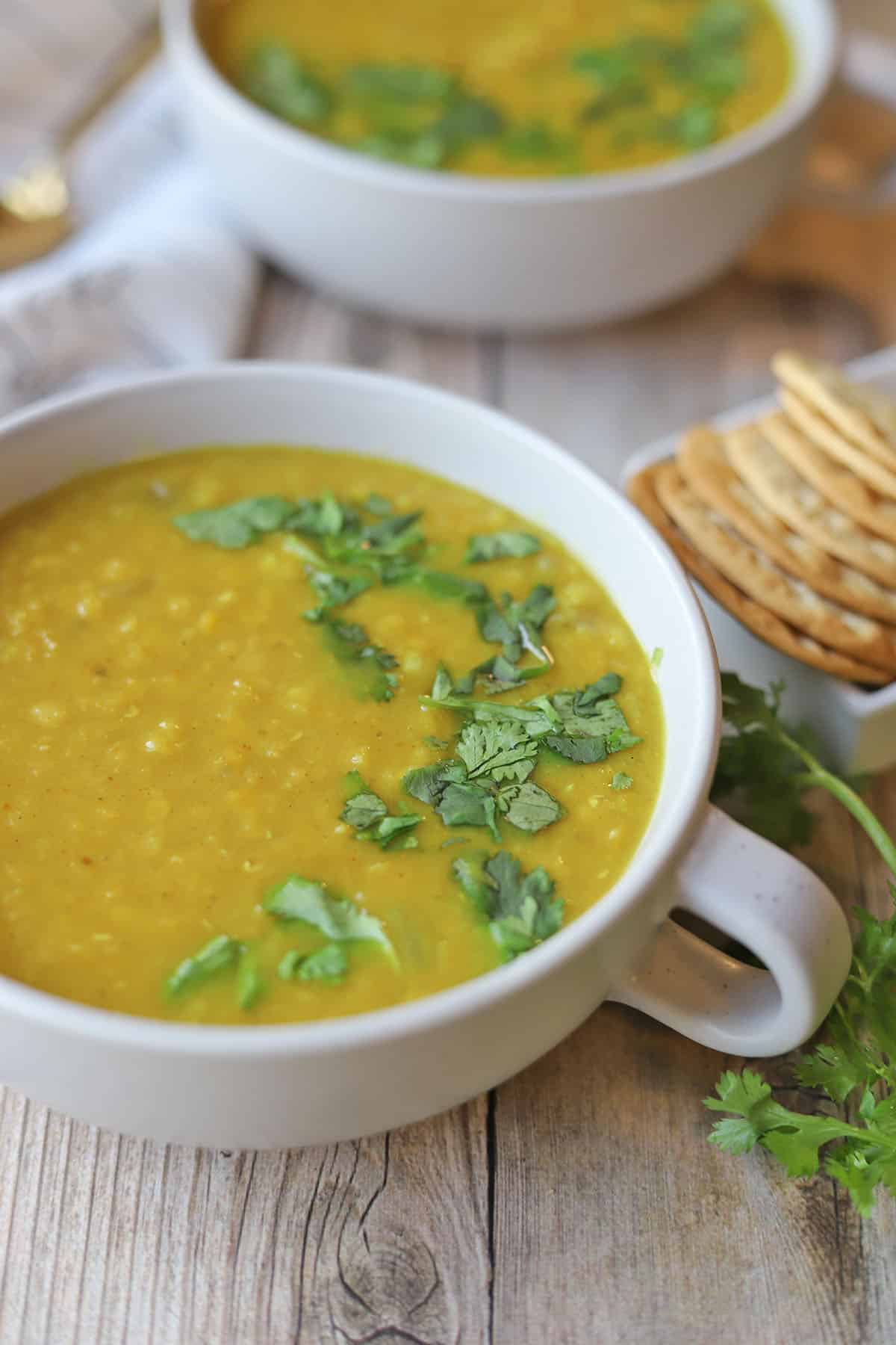 Curried red lentil soup in large white mugs, topped with cilantro.
