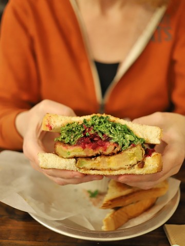 Hands holding fried green tomato sandwich