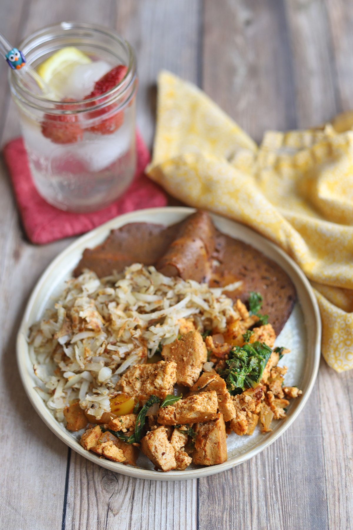 Tofu scramble on plate with hash browns and seitan bacon.