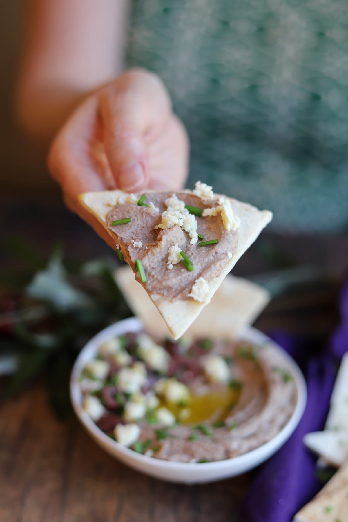 Hand holding pita bread triangle with olive hummus.