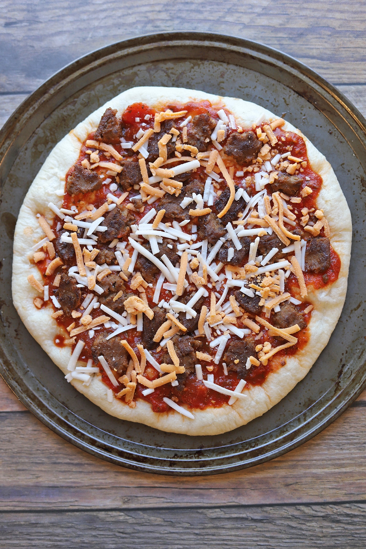 Pizza crust topped with veggie burger and shredded non-dairy cheese.