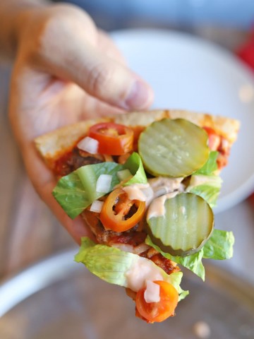 Hand holding slice of vegan cheeseburger pizza.