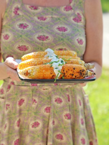Hands holding buffalo grilled corn on the cob.