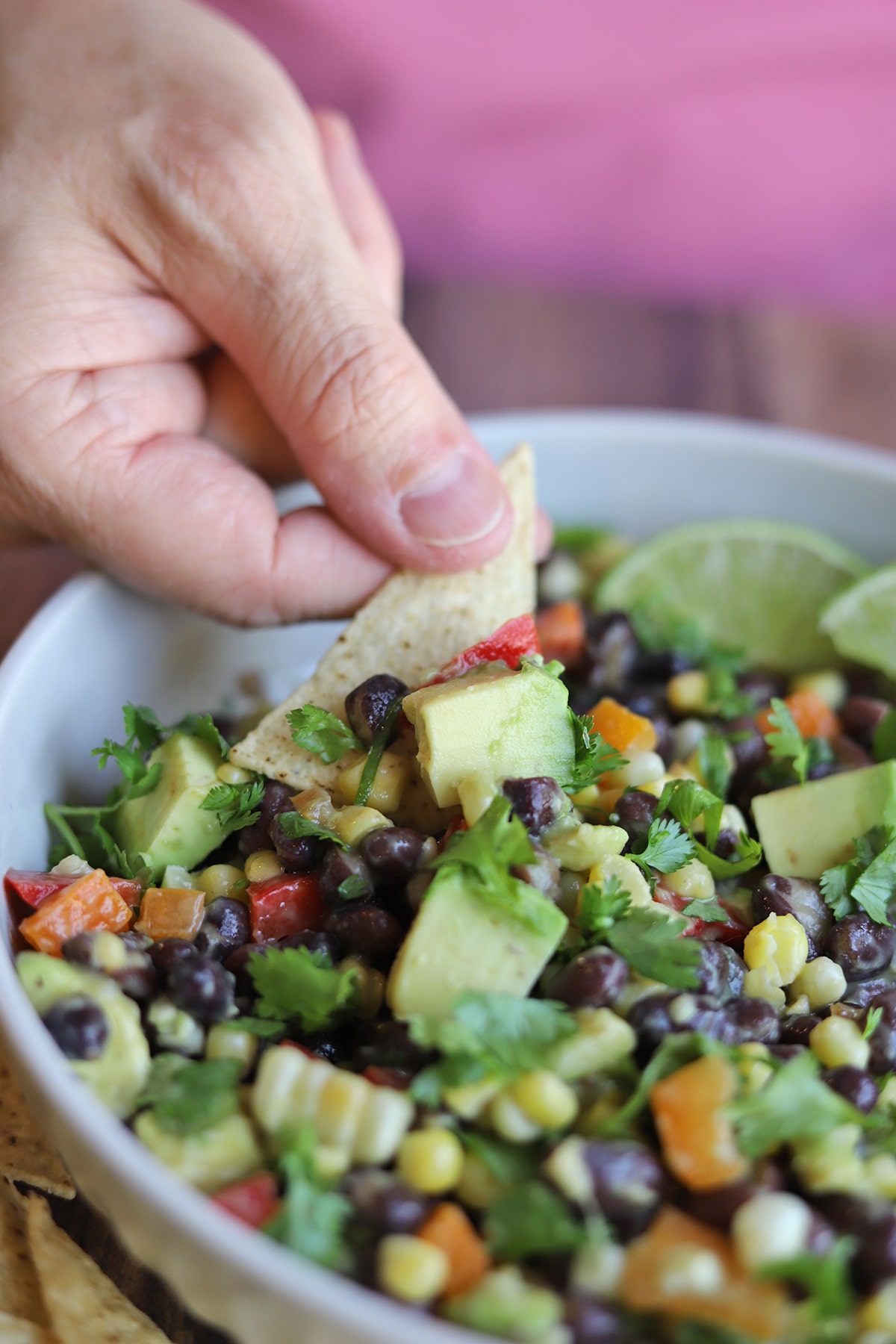 Hand dipping chip into black bean salad with avocado and corn.