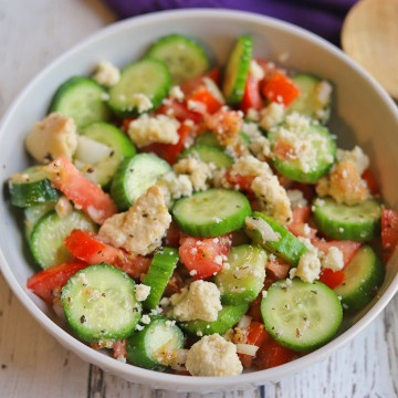 Cucumber tomato salad in bowl by wooden spoon.