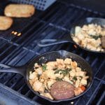 Cast iron skillets on an outdoor grill with tofu scramble and veggie sausage.
