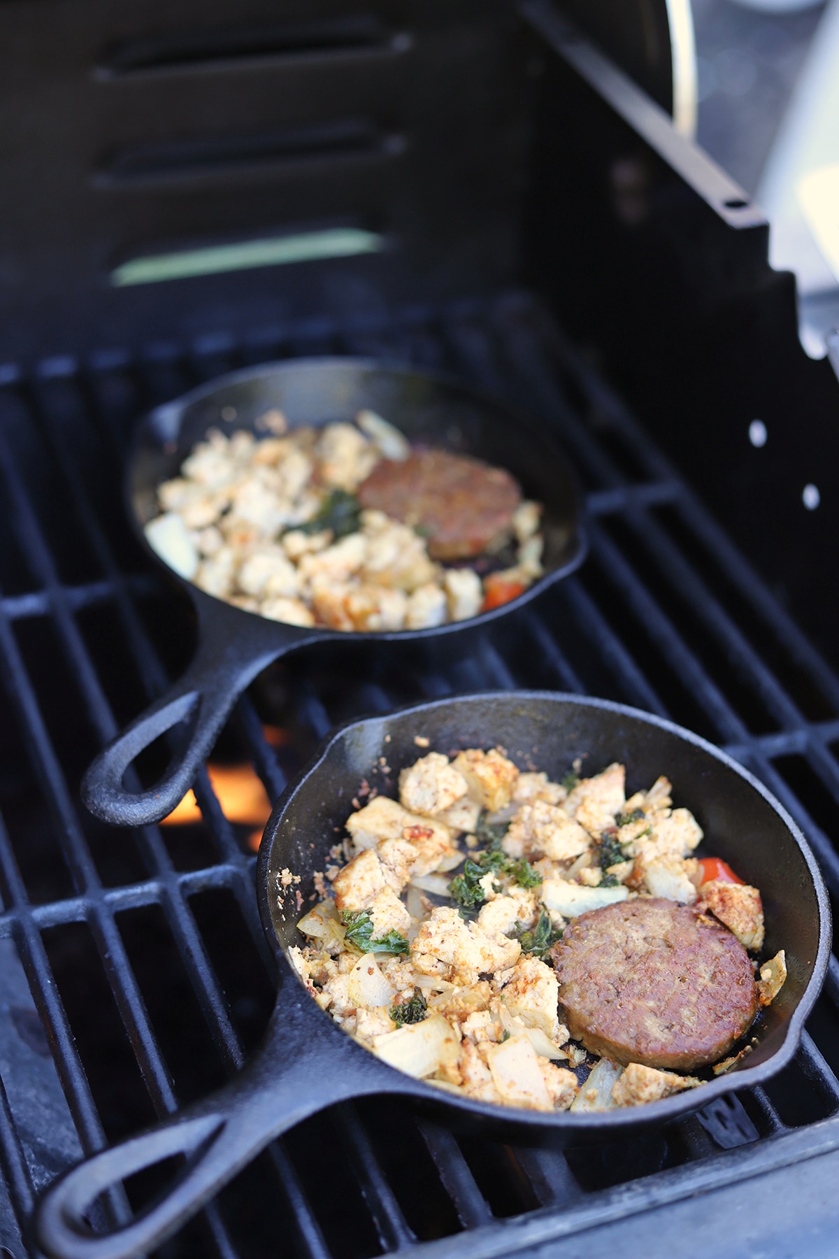 Cast iron breakfast skillets cooking on outdoor grill.