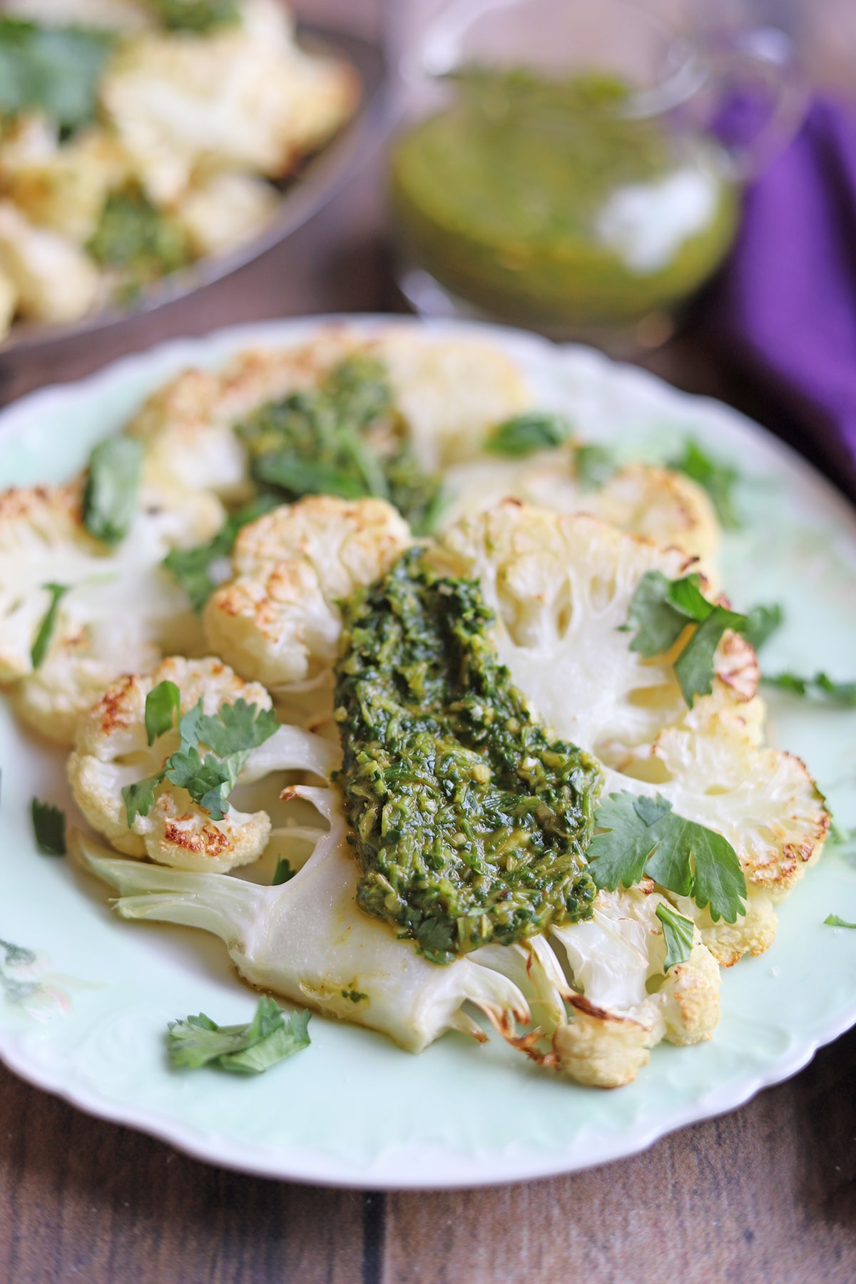 Two cauliflower steaks on plate with chimichurri.