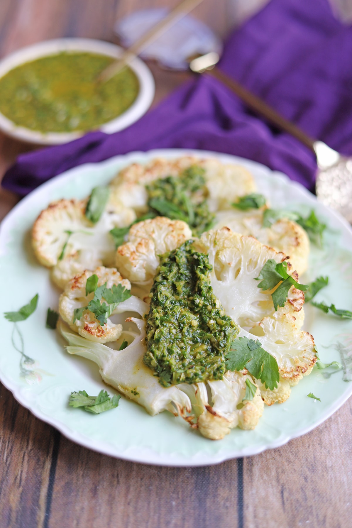 Two cauliflower steaks on plate with cilantro chimicurri.