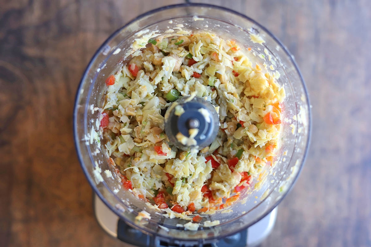 Food processor with blended artichokes, chickpeas, bell pepper, and onions.