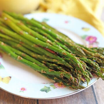Pile of air fried asparagus on floral plate.