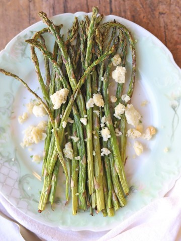 Air fried asparagus on plate with vegan feta cheese crumbled on top.
