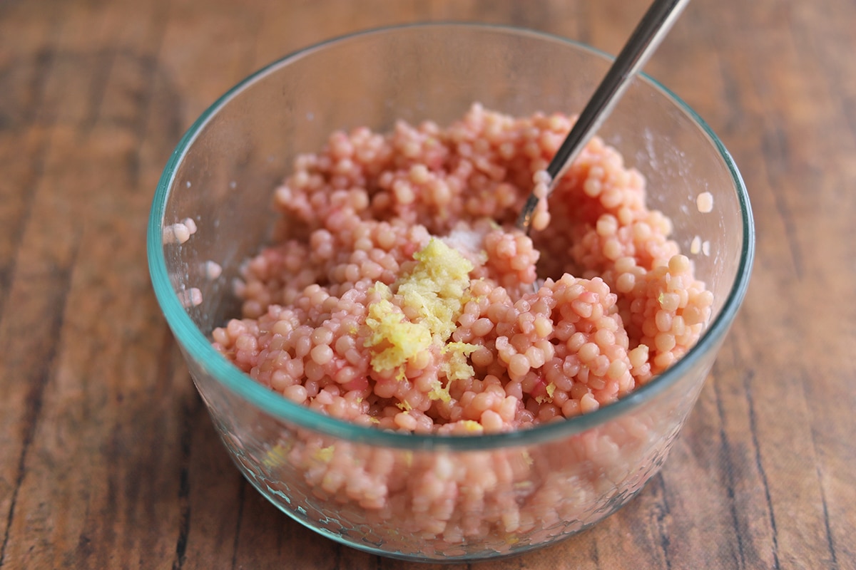 Bowl with pink couscous, zested garlic & lemon, and salt.