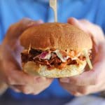 Hands holding barbecued Soy Curls sandwich with coleslaw.