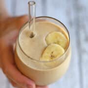 Hand holding peanut butter banana smoothie with sliced banana garnish.