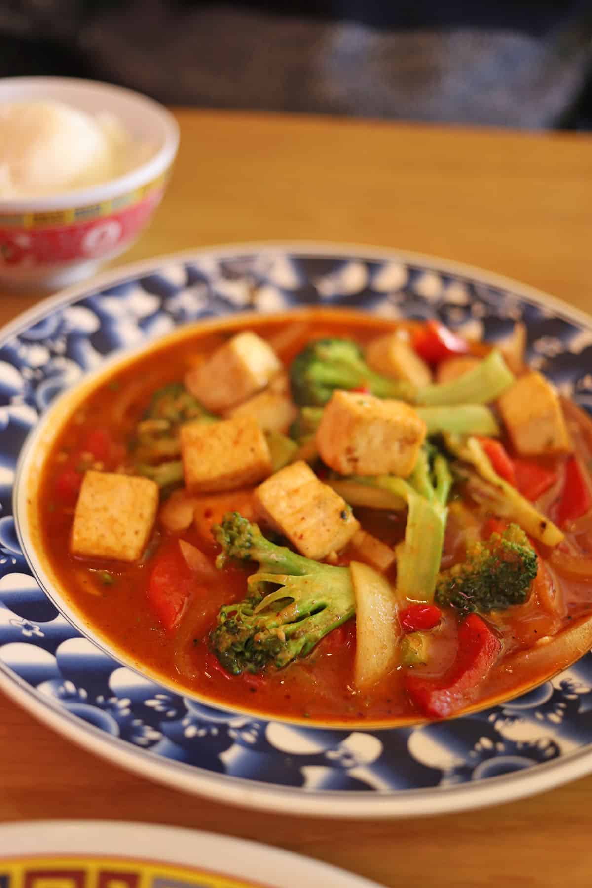 Tofu and broccoli in curry peanut sauce on blue plate.