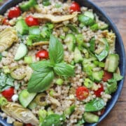 Israeli couscous salad with basil, cucumber, tomatoes, and artichoke hearts in blue bowl.