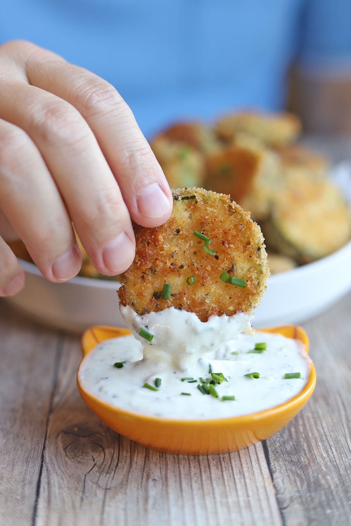 Hand dipping breaded zucchini chip into ranch dressing.