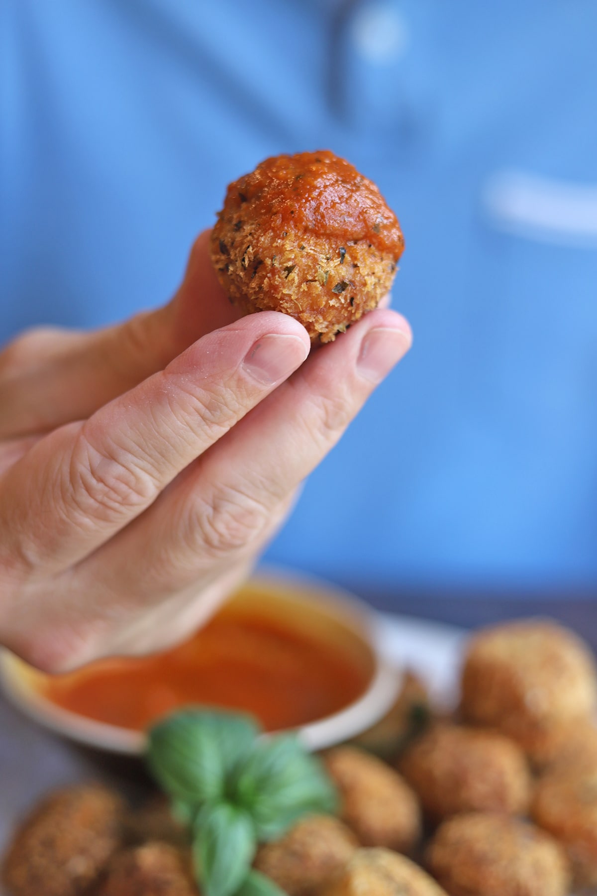 Hand holding cheese ball topped with marinara.