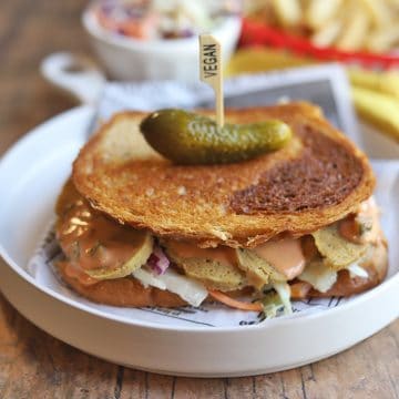 Toasted sandwich on plate & topped with a pickle.