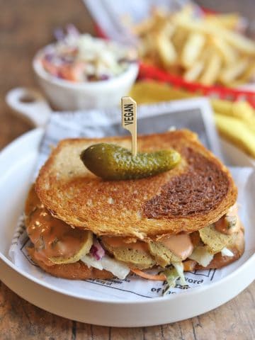 Toasted Rachel sandwich with seitan chicken on plate and topped with a pickle.