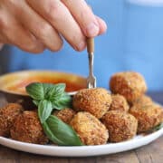 Fried almond cheese balls with fresh basil by bowl of marinara for dipping.