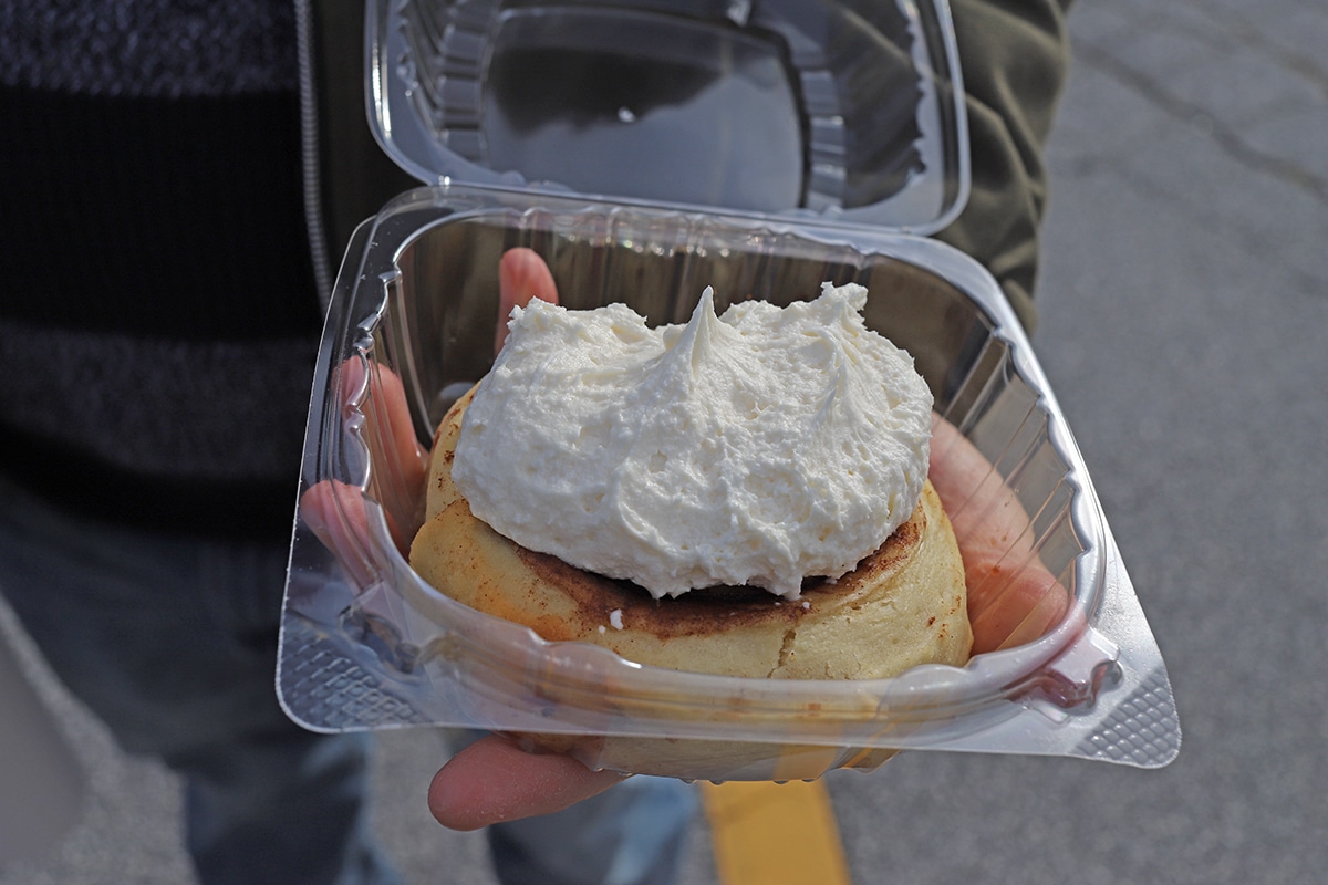 Hand holding cinnamon roll in plastic container.